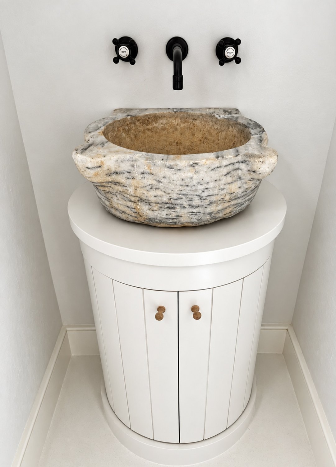 Curved beadboard vanity beneath an antique carved stone basin